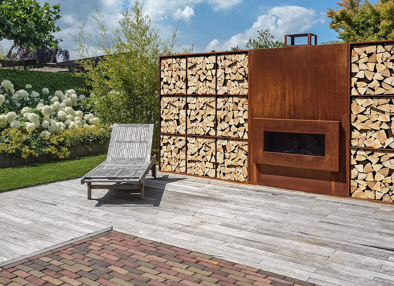 Cortenstahlregal mit Rückwand als Sichtschutz auf der Terrasse, befüllt mit Brennholz, freistehend in Edelrost-Optik im Außenbereich.