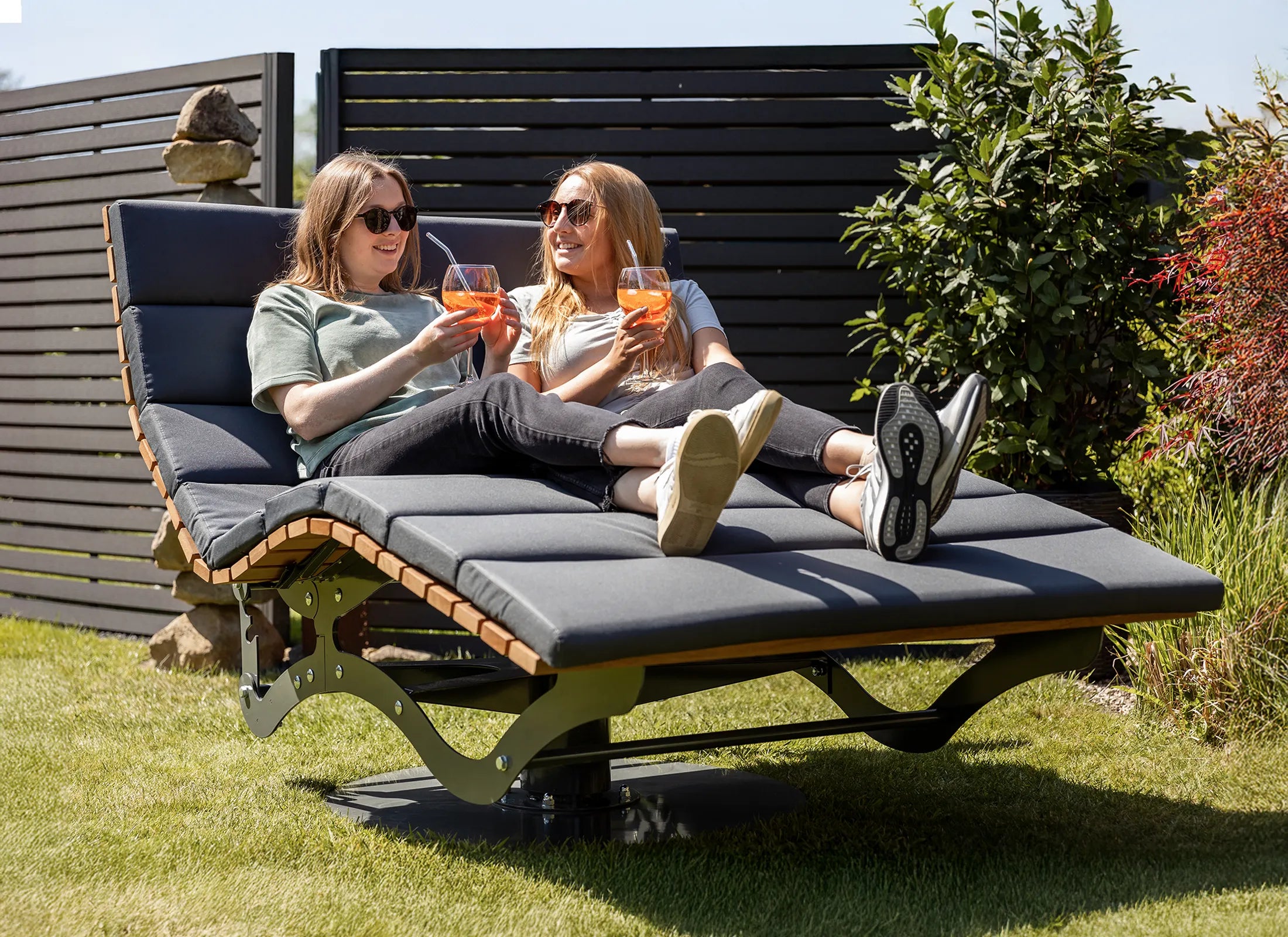 Dreh-Waldsofa von Liegeland mit Polsterauflage und Personen, 360° drehbare Garten-Doppelliege und verstellbare Outdoor-Ruheinsel im natürlichen Außenraum.