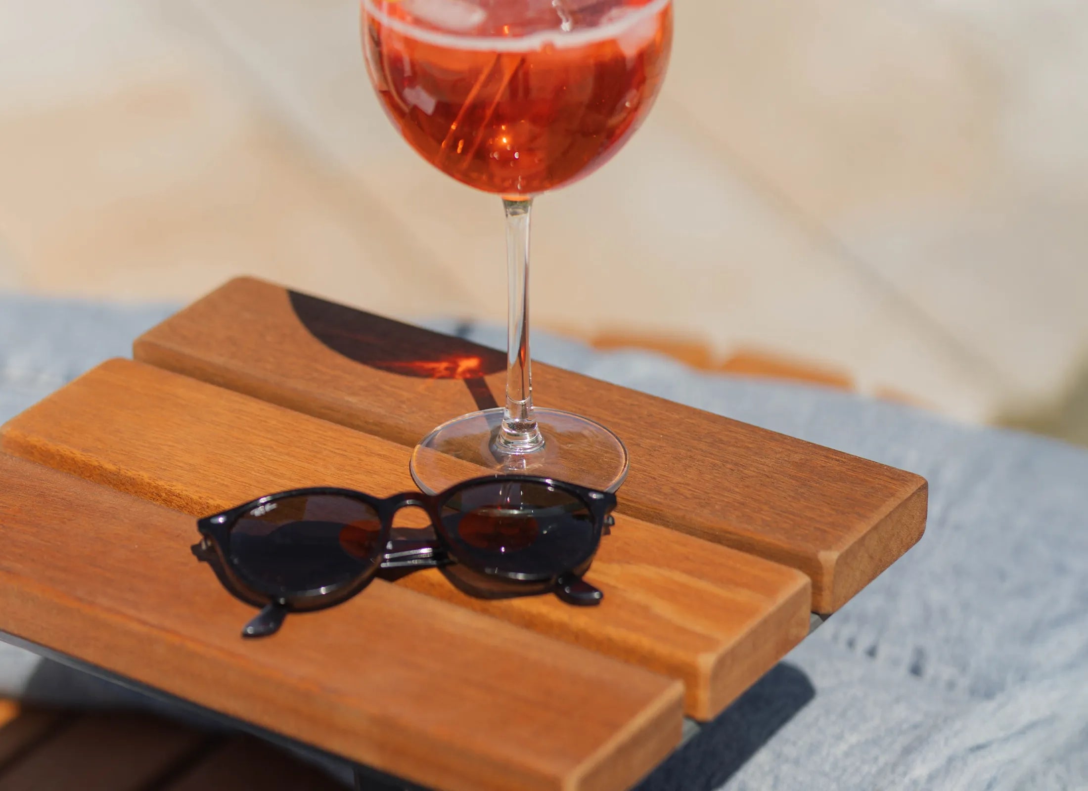 Waldsofa Gegenüberliegend mit montiertem Ablagetisch – elegante Holzliege, Relaxliege und Designliege im privaten Garten, Sonnenbrille und Aperol Spritz