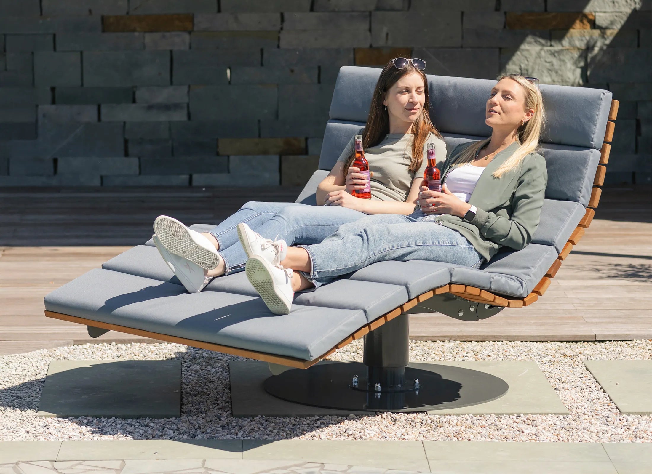 Waldsofa Drehbar von Liegeland aus Bangkirai mit Grundplatte und Polstern, 360° Drehliege und komfortable Panoramaliege mit Personen als Outdoor-Ruheinsel im Garten.
