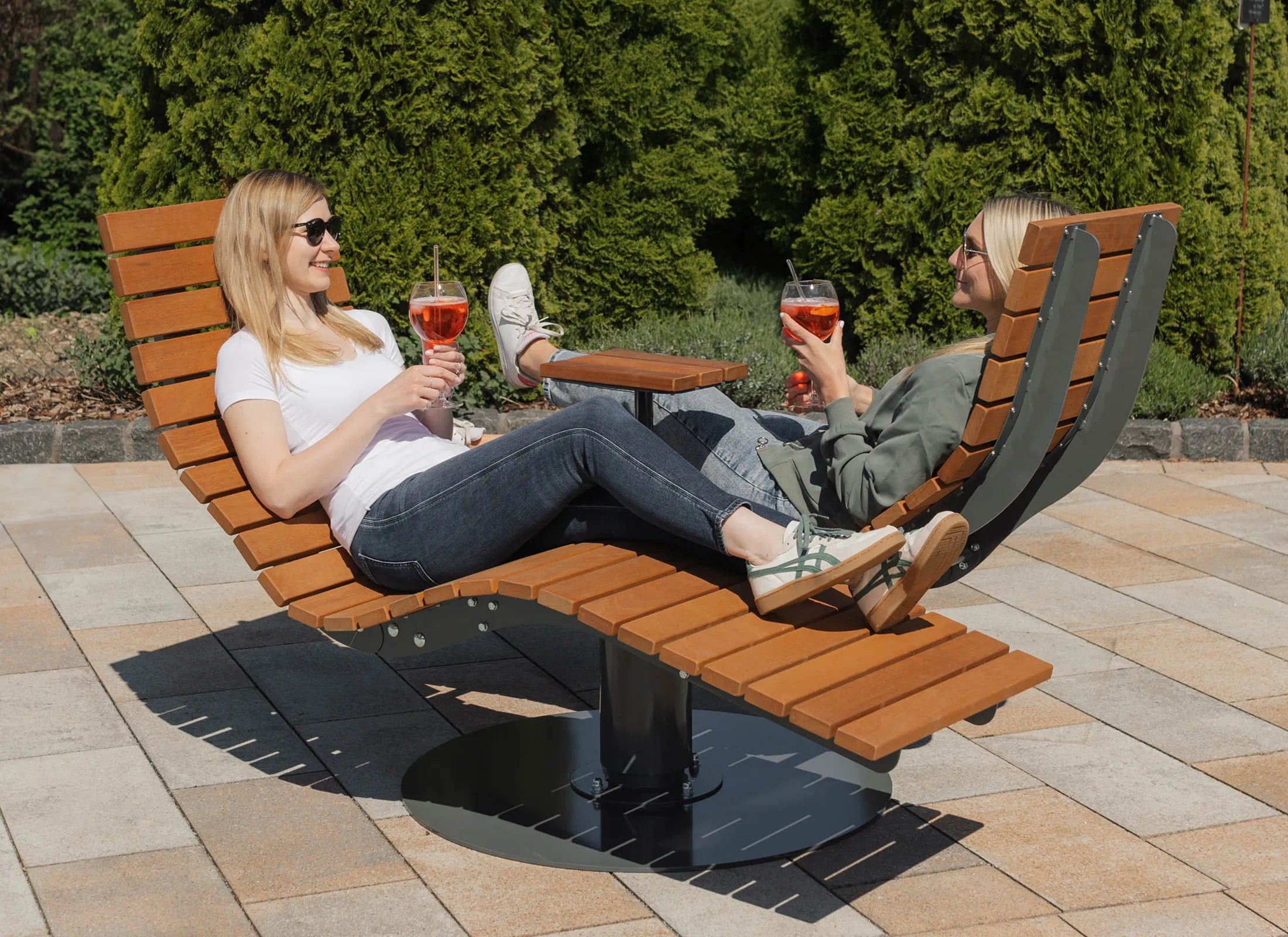 Waldsofa Gegenüberliegend von Liegeland als 360° drehbare Panorama-Liege und Wellnessliege, kommunikative Wellenliege und Waldliege mit Personen im Park oder Garten.