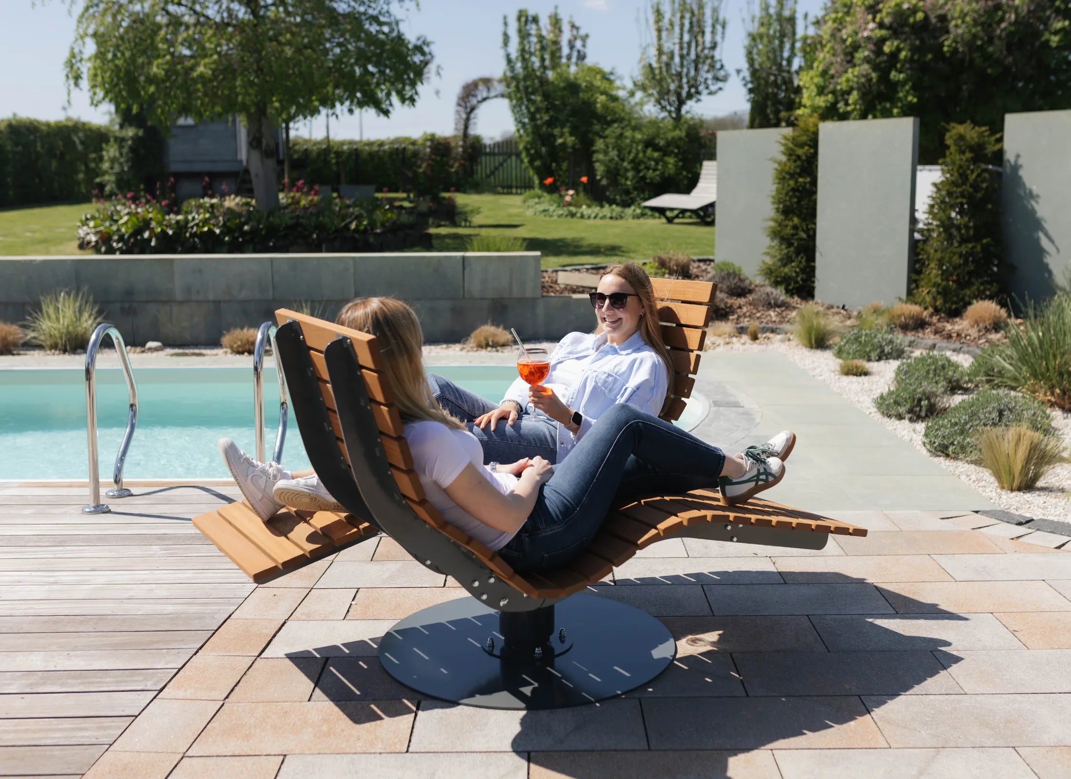 Waldsofa Gegenüberliegend von Liegeland als rotierende Waldliege und Design-Wellenliege, großzügige Wellnessliege und Kommunikationsliege im Außenbereich mit Personen.